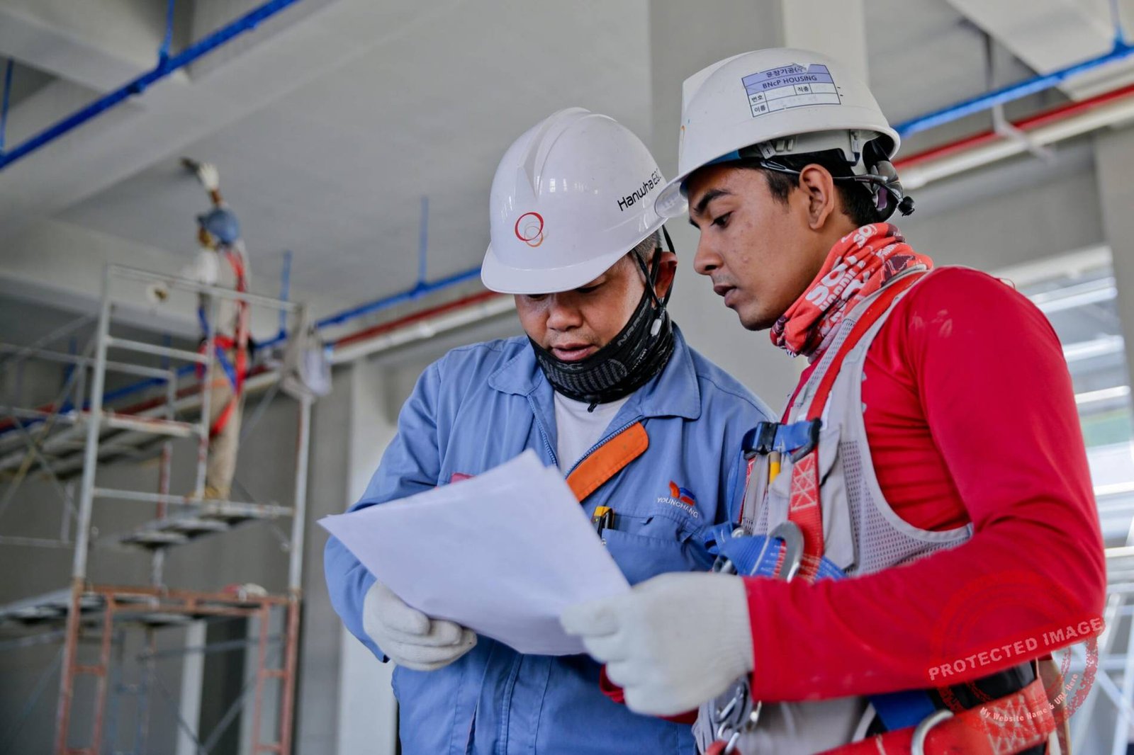 Two engineers in safety helmets reviewing construction plans at a worksite.